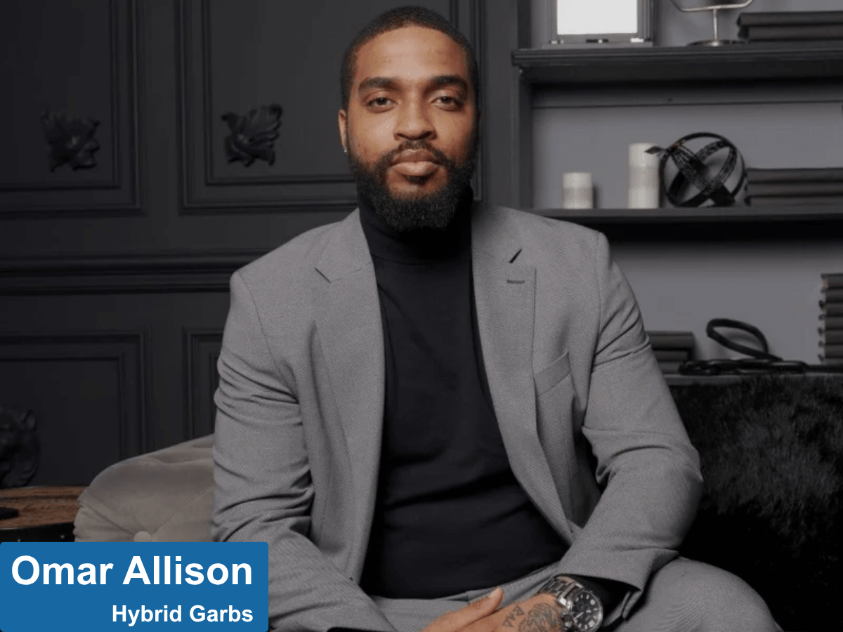 black man in a grey-brown suit sitting in living room