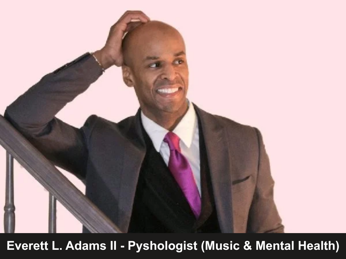 black man in brown suit leaning on stair railing